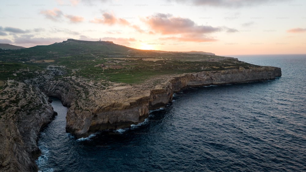 the sun is setting over the ocean near a rocky cliff
