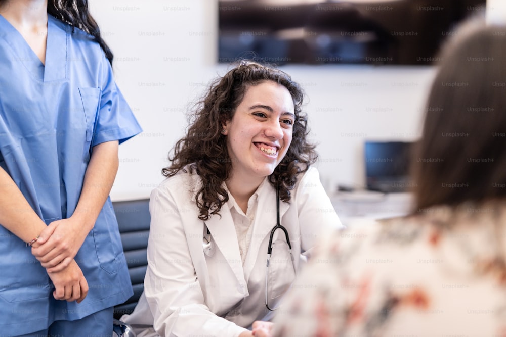 Una mujer en batas sentada en una mesa hablando con una enfermera