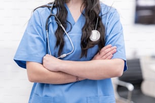 Una donna in scrub e uno stetoscopio in piedi con le braccia incrociate