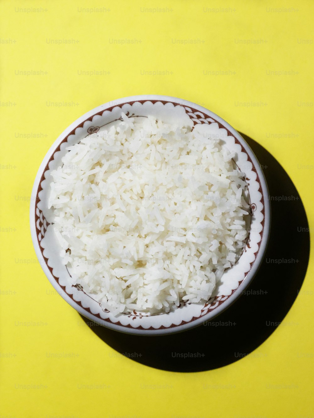 eine Schüssel mit weißem Reis auf gelbem Hintergrund