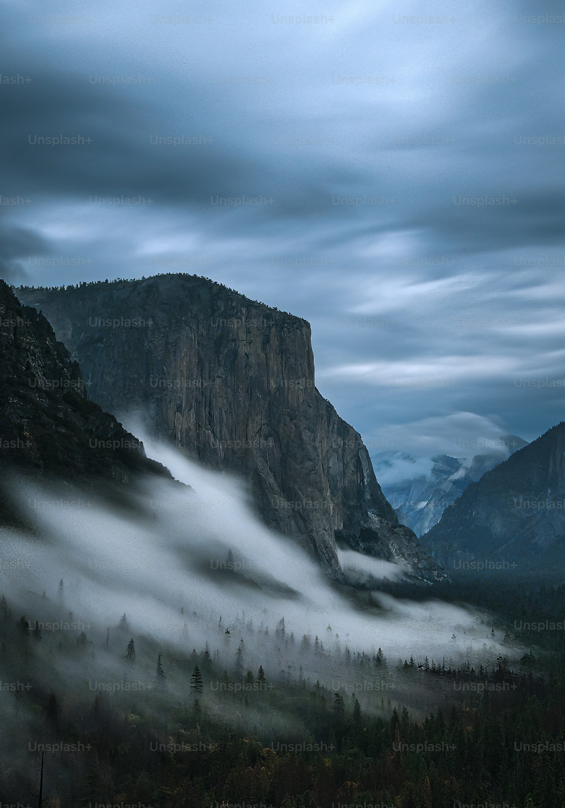 a mountain covered in fog with a forest below