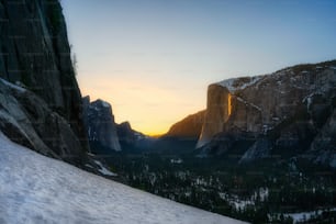 the sun is setting over the mountains with snow on the ground