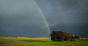 uma casa em um campo com um arco-íris no fundo