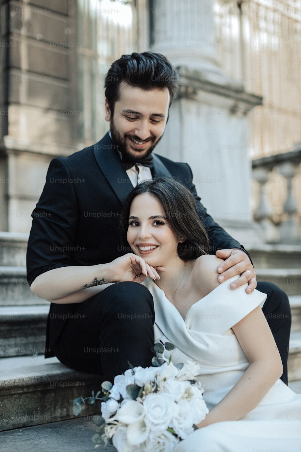 a bride and groom sitting on the steps of a building
