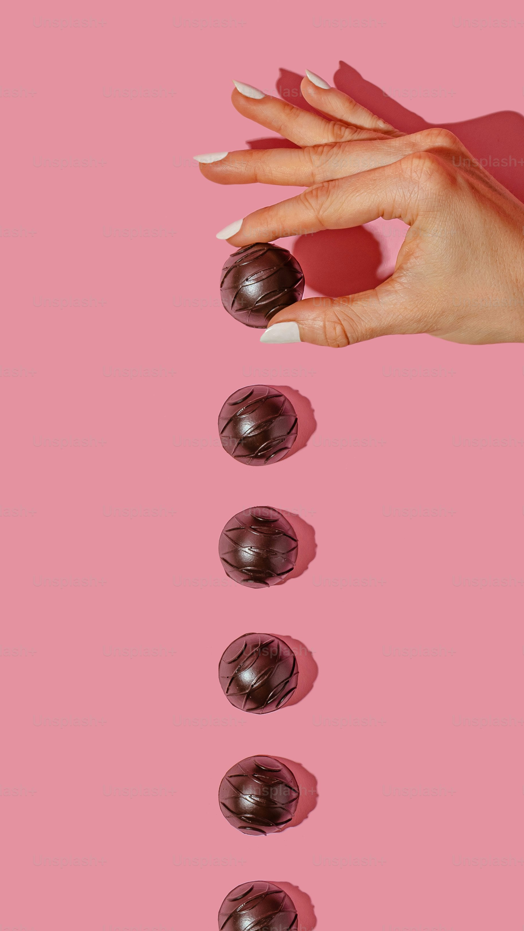 분홍색 배경에 매니큐어와 초콜릿을 가진 여자의 손
