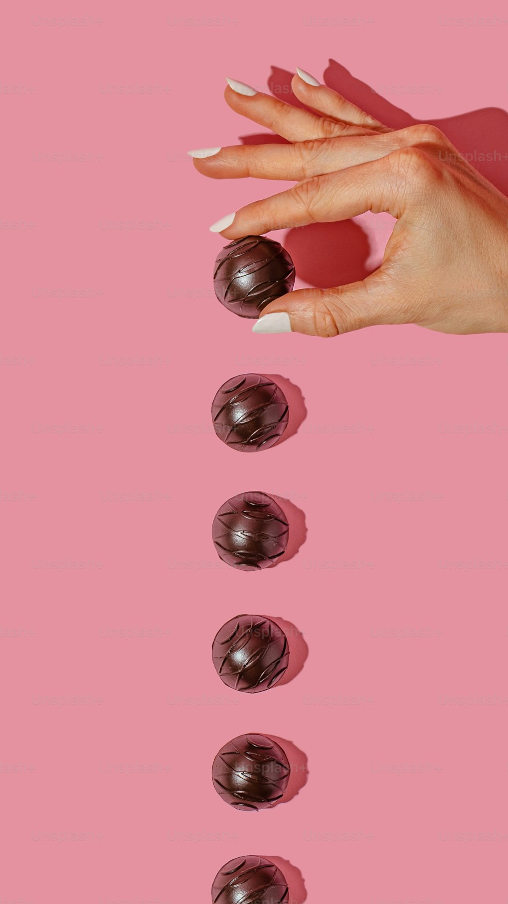 ピンクの背景にマニキュアとチョコレートを持つ女性の手