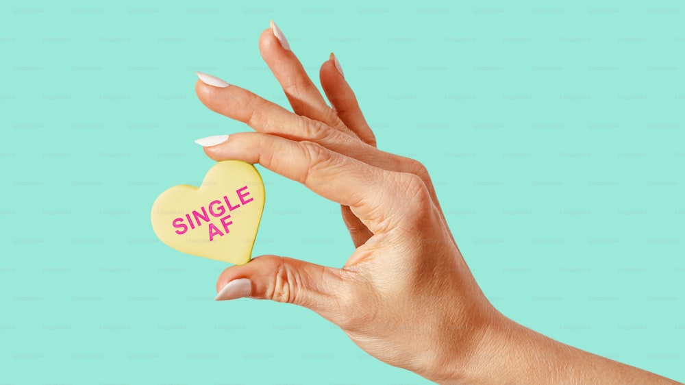 a woman's hand holding a candy heart with the word single af on it