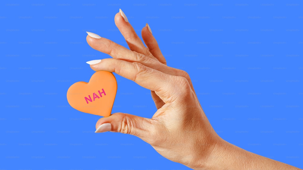 Eine Frauenhand, die ein orangefarbenes Herz mit dem Wort Han darauf hält
