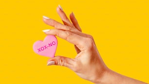 a woman's hand holding a pink heart shaped cookie