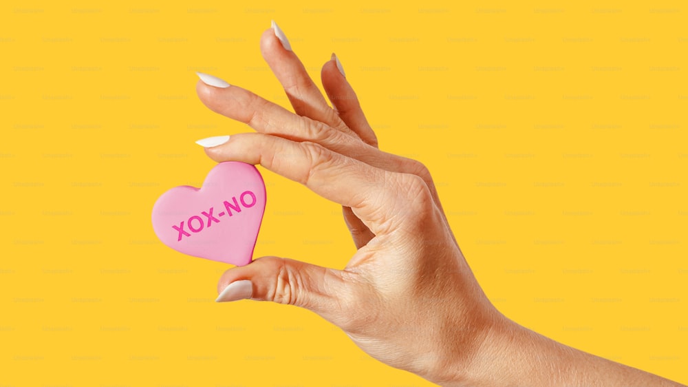 Une main de femme tenant un biscuit rose en forme de cœur