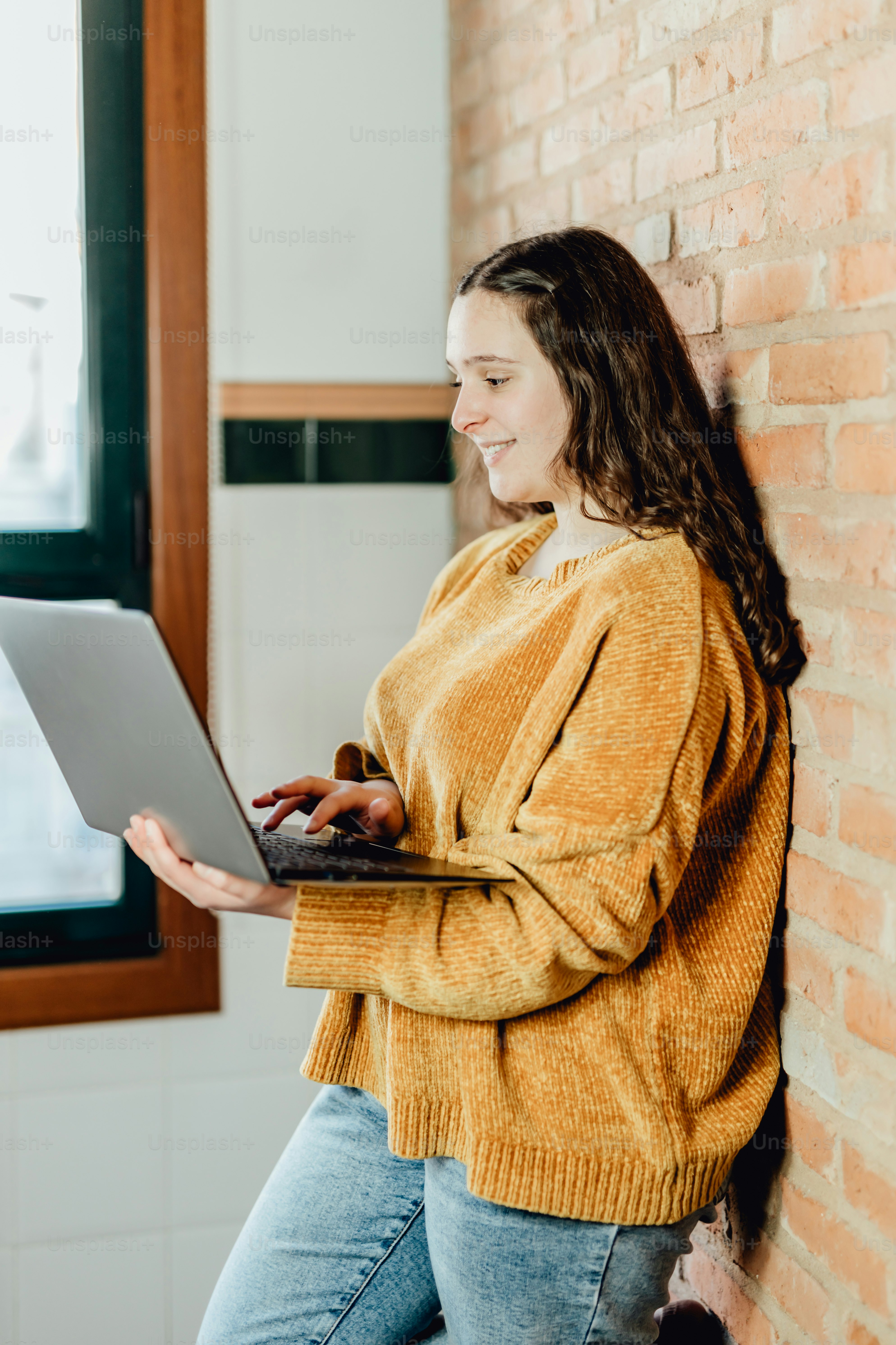 uma mulher que está ao lado de uma parede de tijolos usando um computador portátil