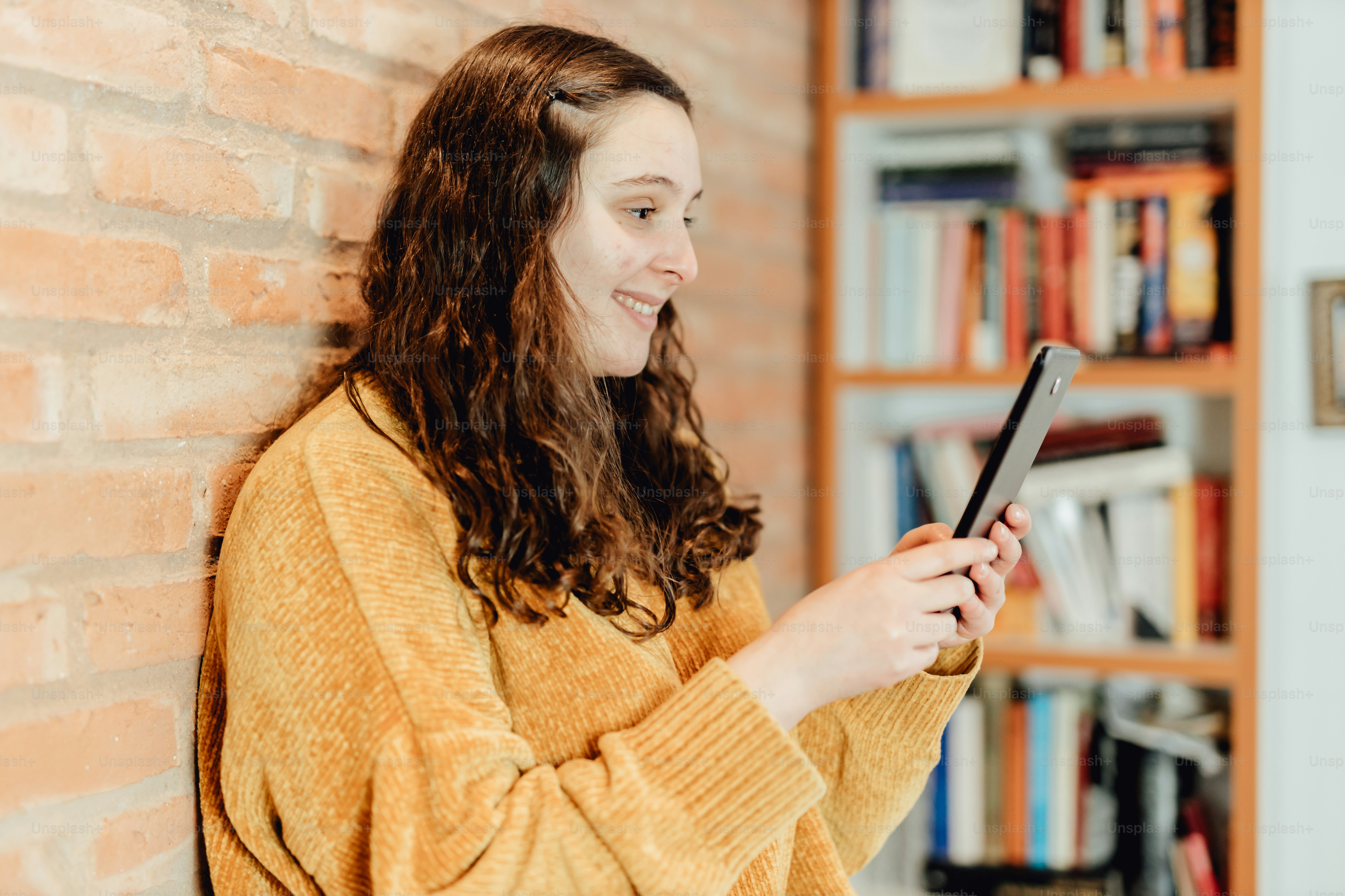 uma mulher de pé ao lado de uma parede de tijolos segurando um tablet