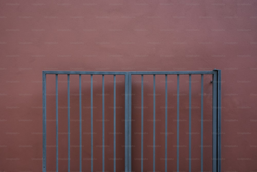 uma parede vermelha com um portão de metal e um gato sentado no chão
