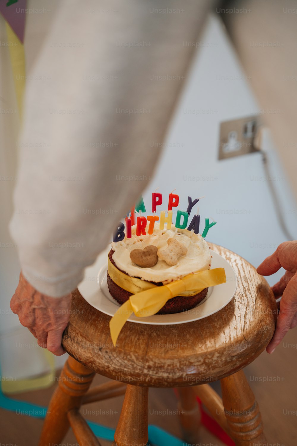 a person holding a birthday cake on a stool