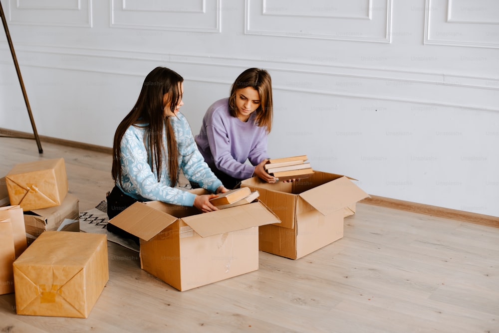 two girls are sitting on the floor with boxes
