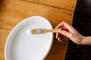 a person holding a paint brush over a white bowl