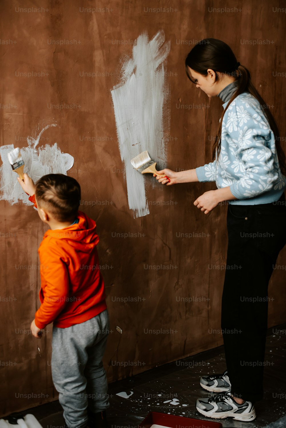 a woman and a child painting a wall