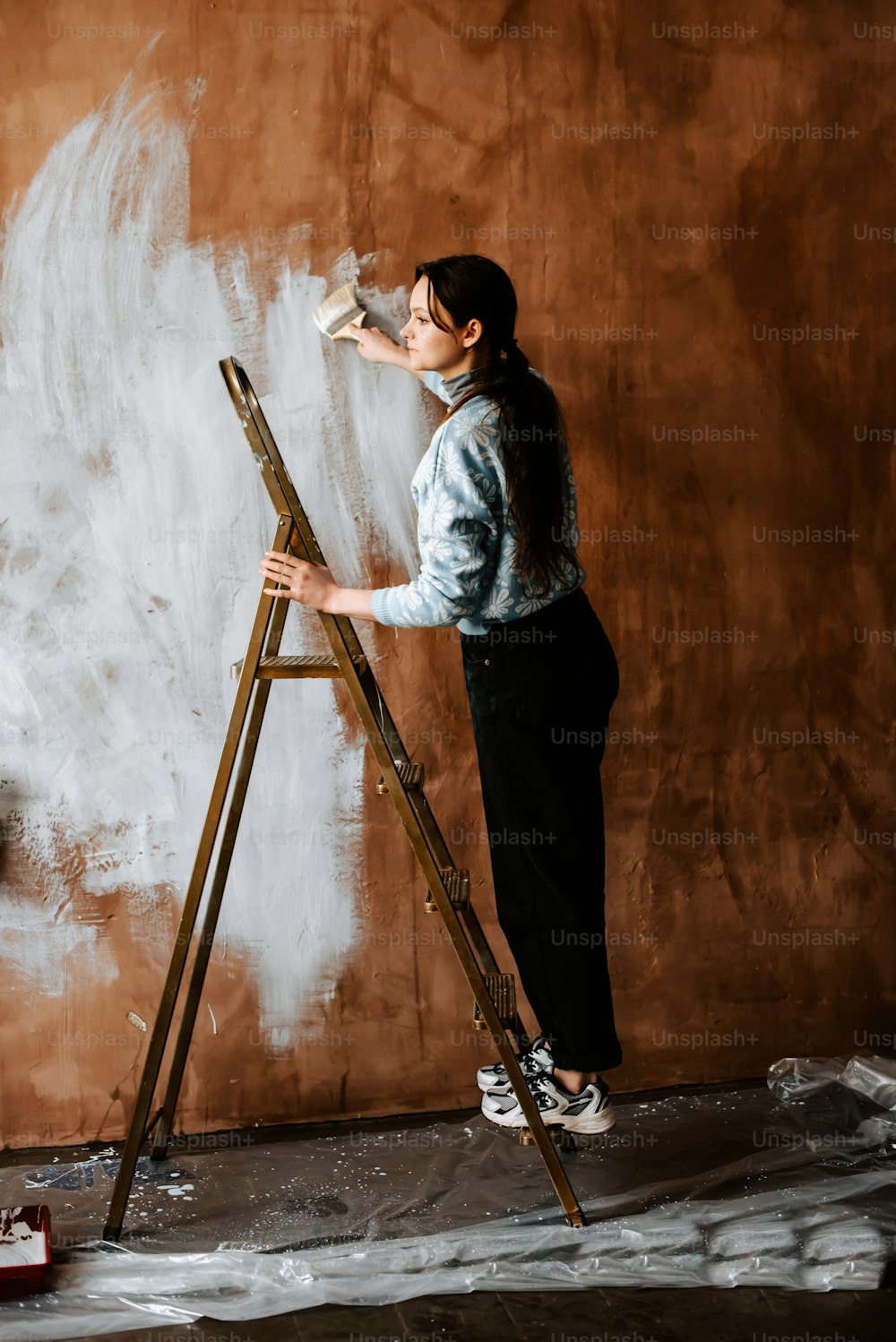 a woman standing on a ladder painting a wall