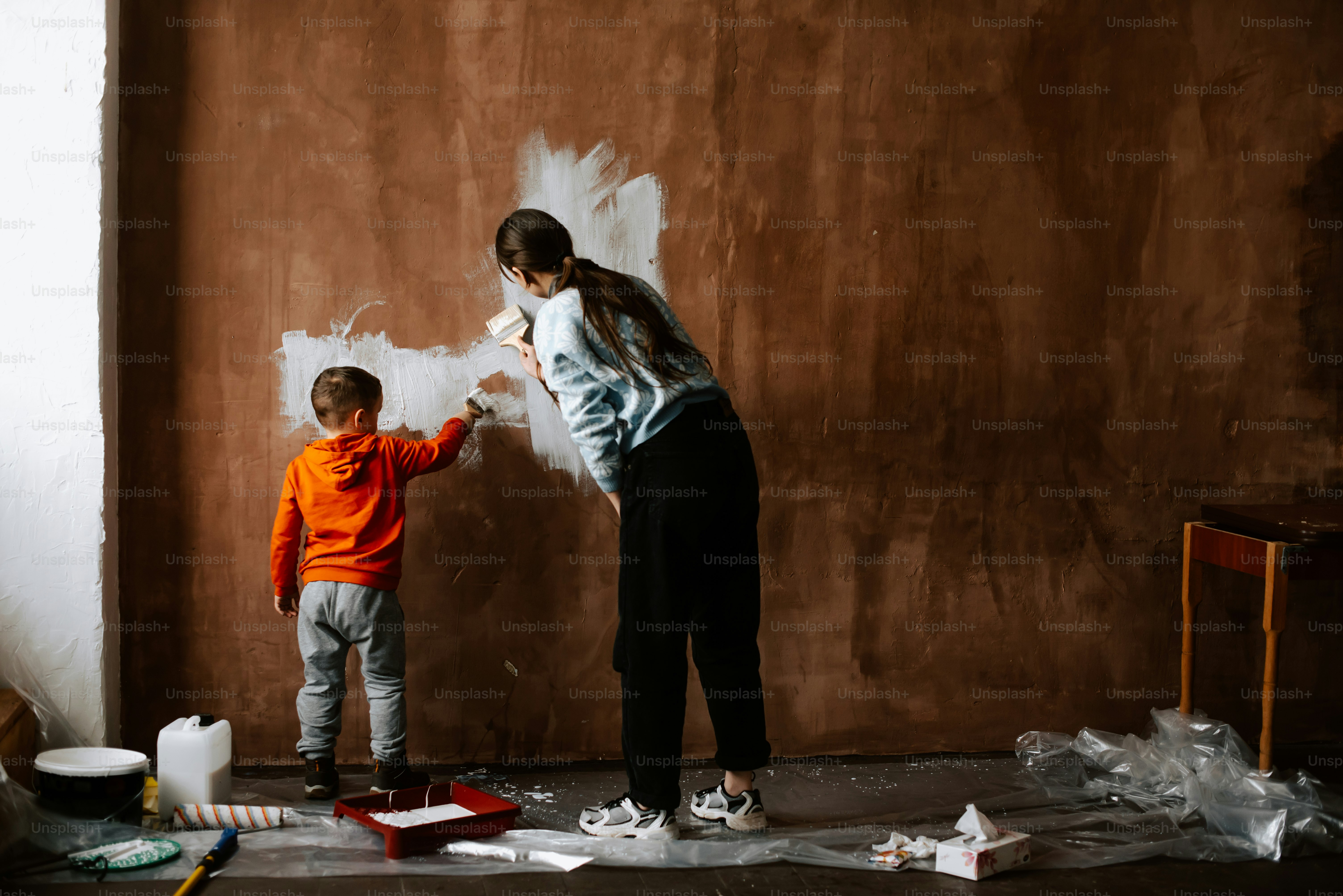 a woman and a child painting a wall