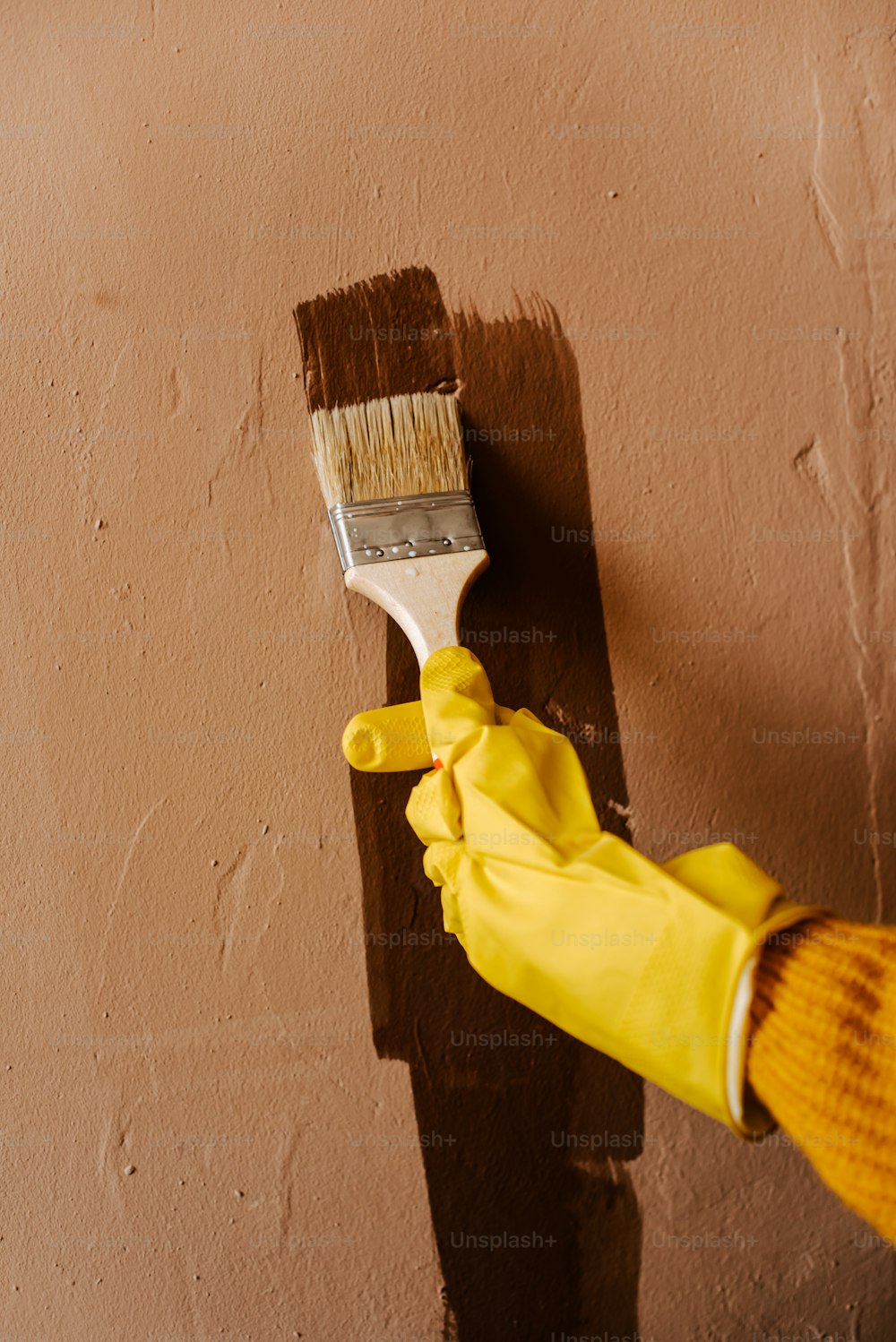 a person in yellow gloves painting a wall with a paintbrush
