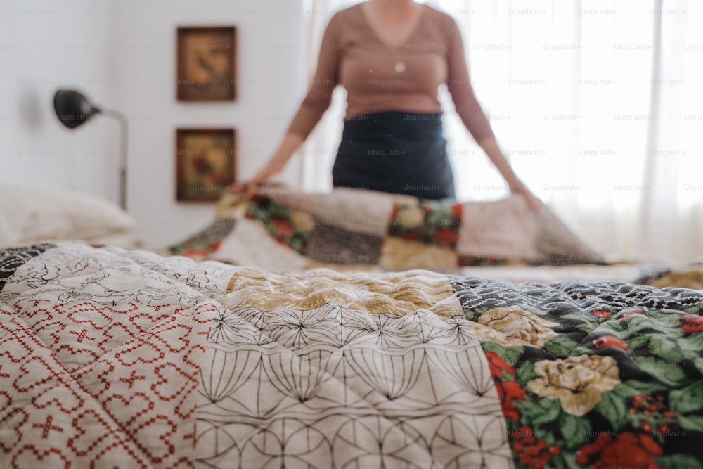 a woman standing in front of a bed with a quilt on it