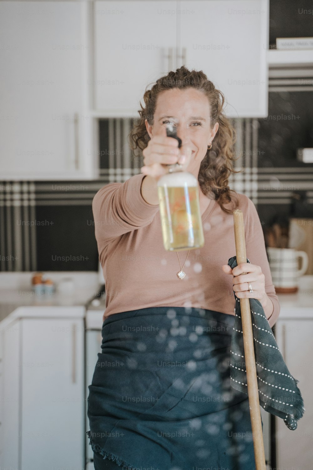 a woman in a kitchen with a broom and a mug