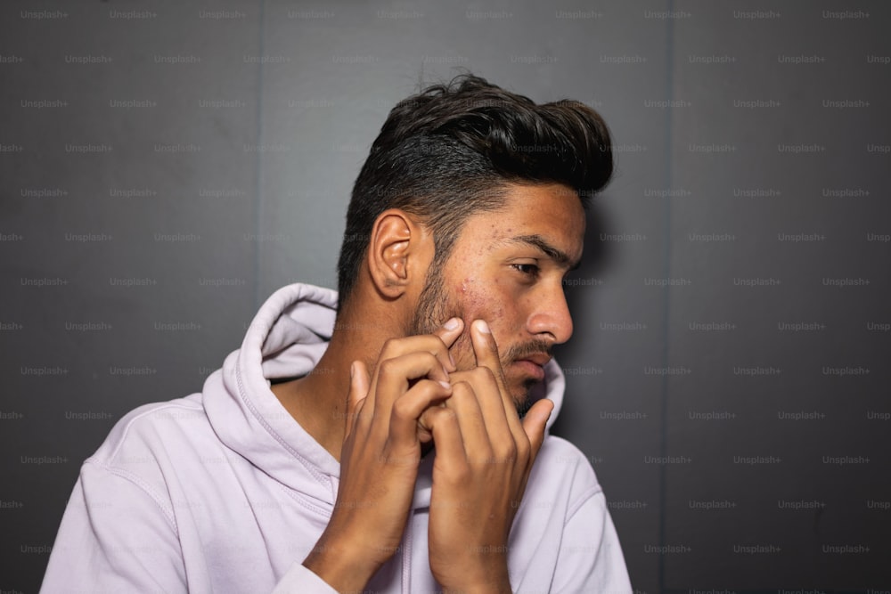 Ein Mann mit Spitzbart und Kapuzenpulli rasiert sich das Gesicht