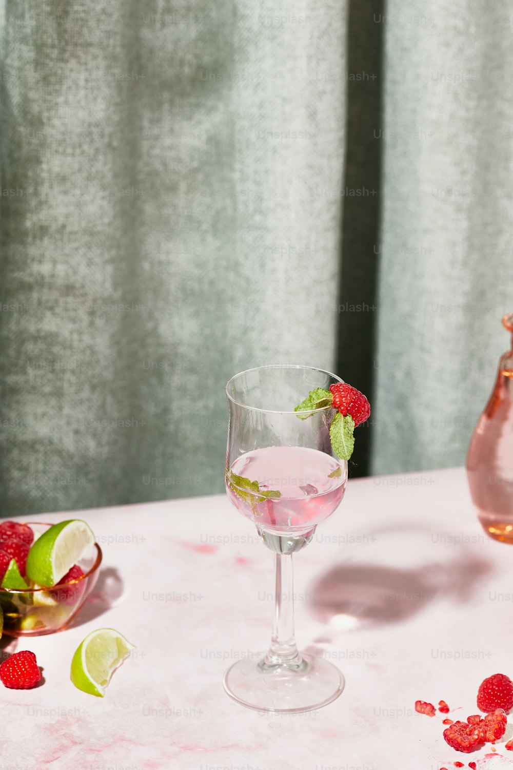 a glass of raspberry lemonade next to a pitcher of raspberry