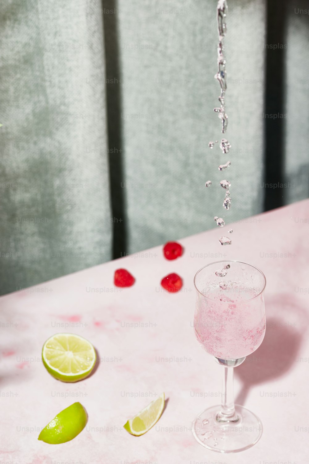ein rosa Tisch mit einem Glas Wasser und Limetten