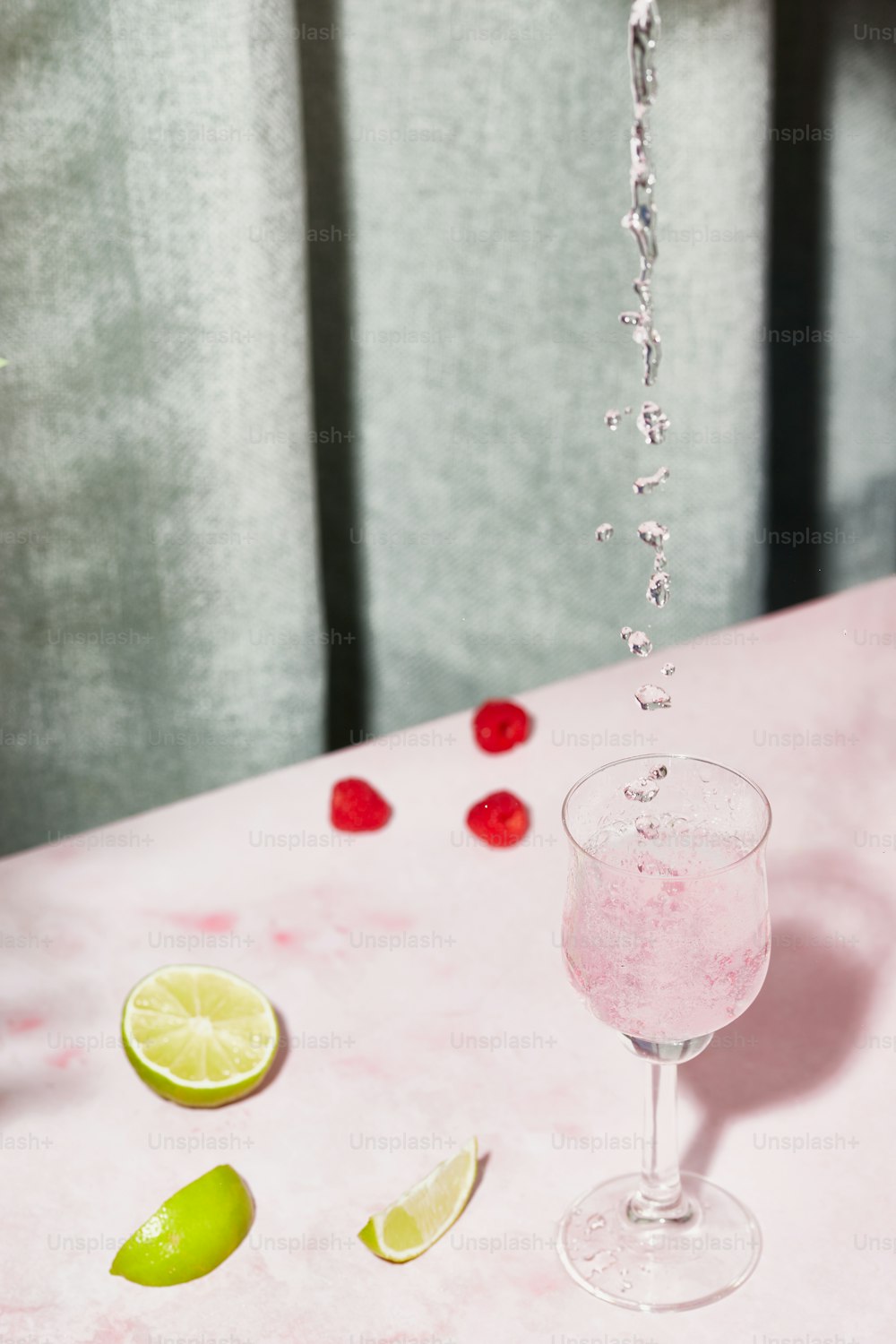 a pink table with a glass of water and limes