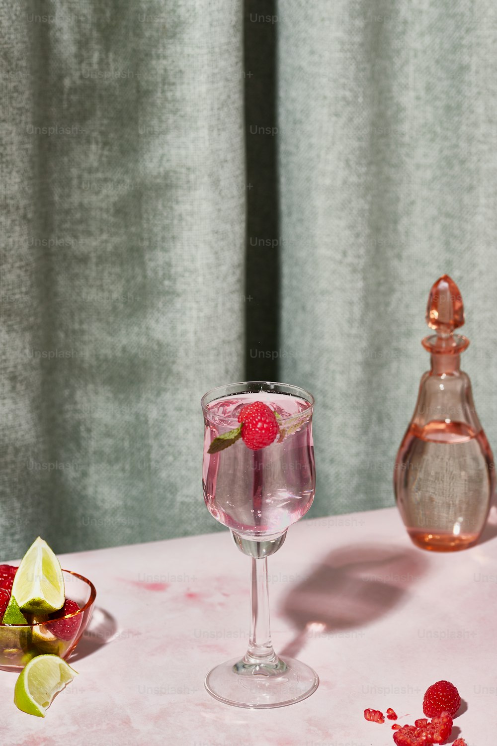 a glass of water with raspberries and limes on a table
