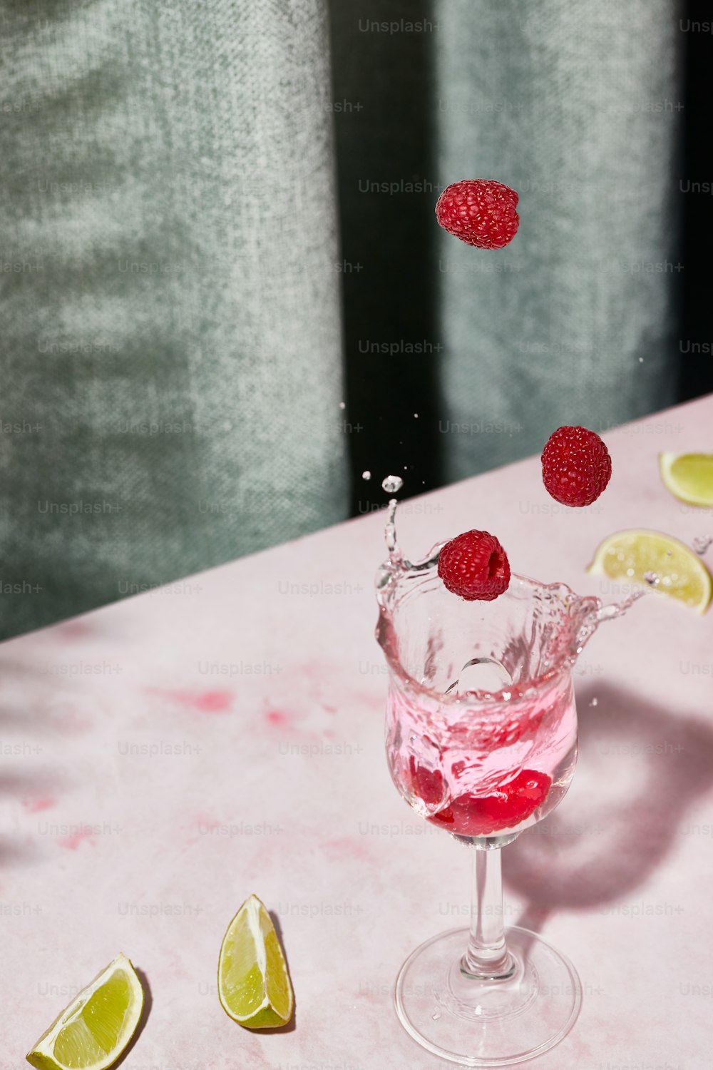 un verre rempli d’un liquide rose et garni de framboises