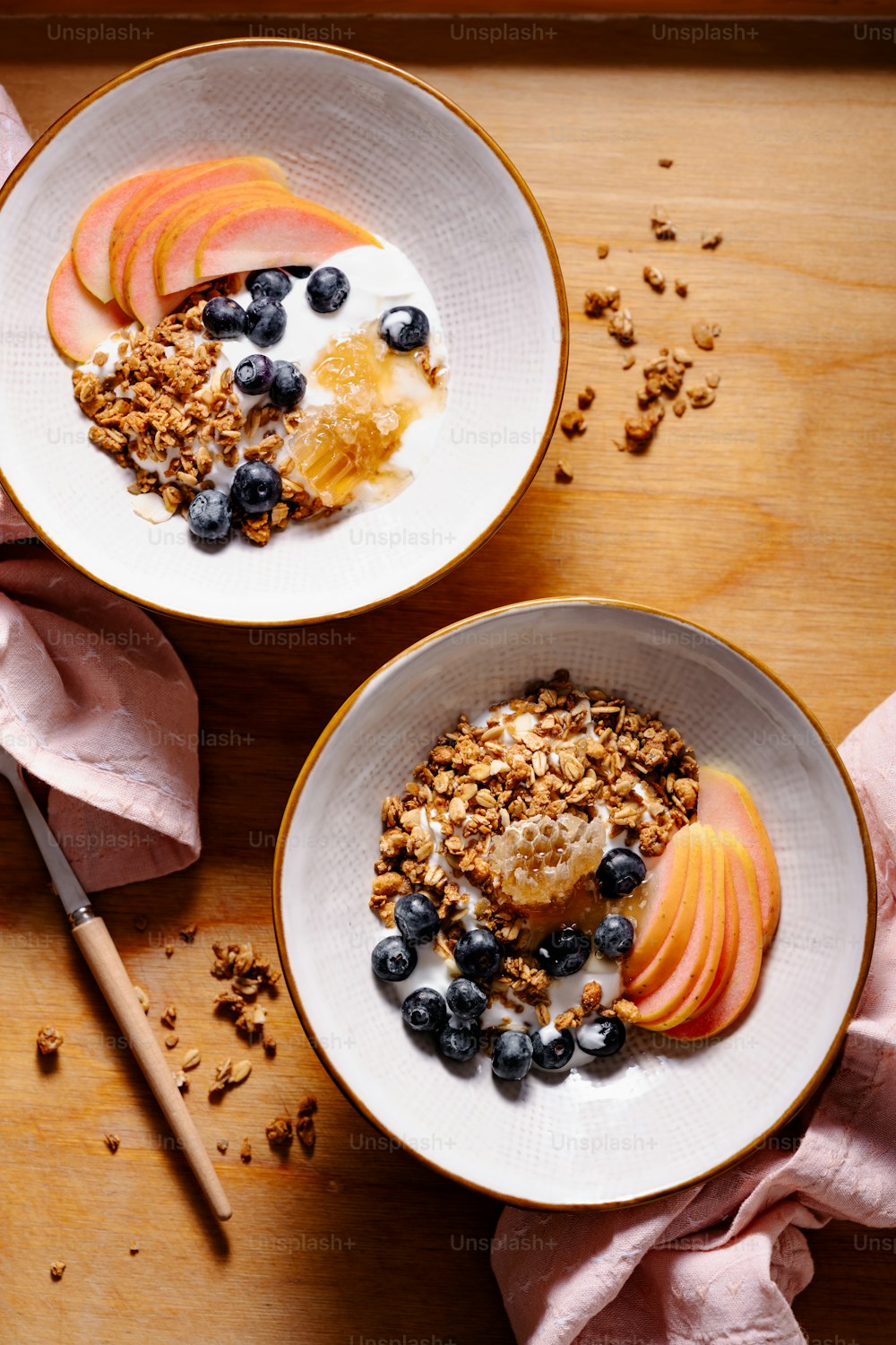 two bowls filled with granola and fruit on top of a wooden table