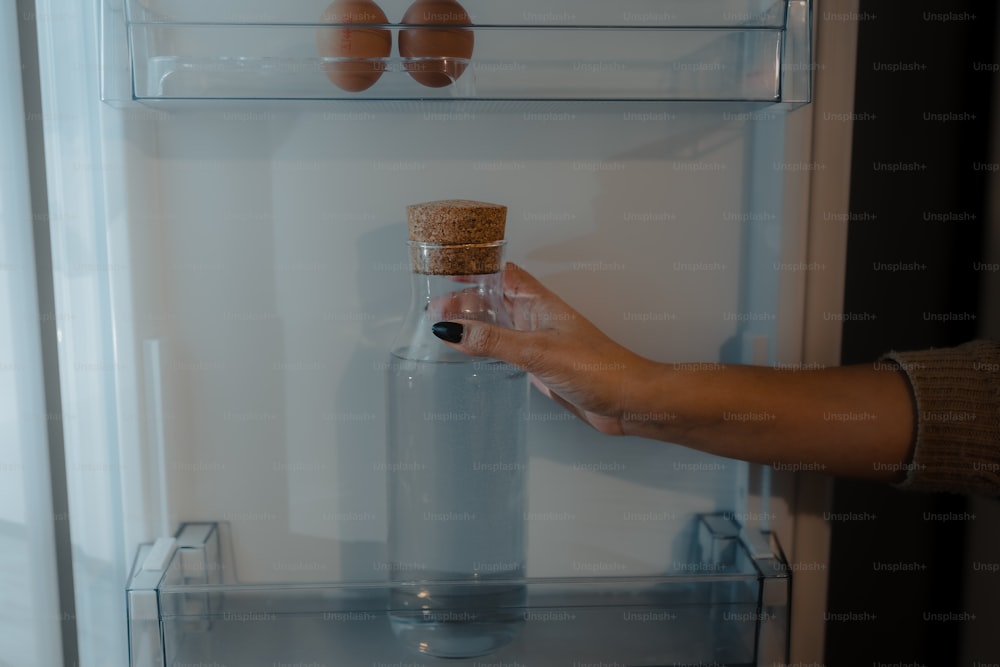 uma pessoa segurando uma garrafa na frente de uma geladeira