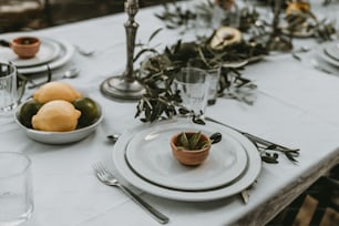 a table set with plates, silverware and a bowl of fruit