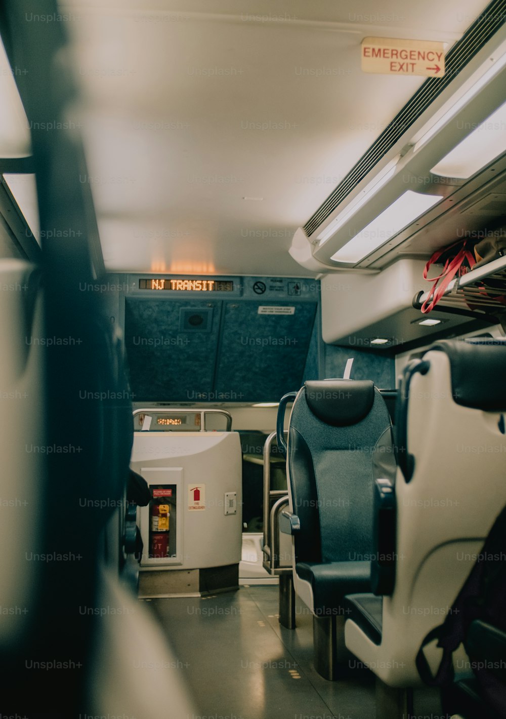 uma vista do interior de um ônibus com assentos e sinais de saída de emergência