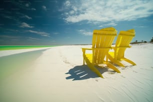 a couple of yellow chairs sitting on top of a sandy beach