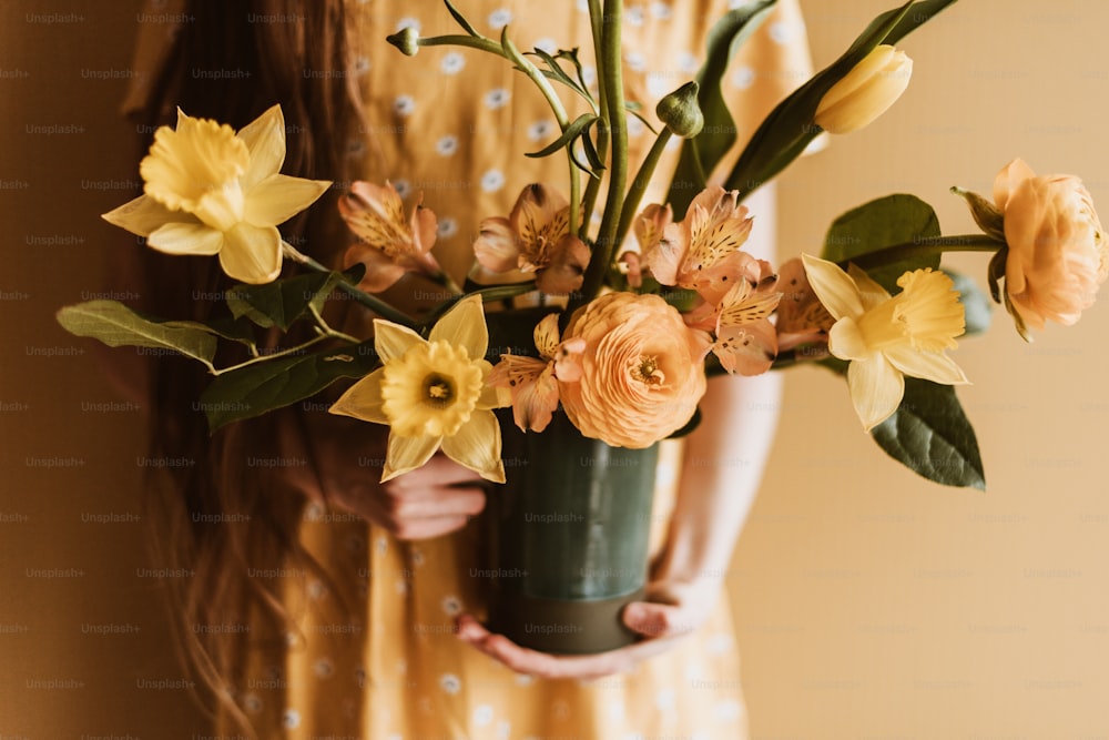 Une femme tenant un vase rempli de fleurs jaunes