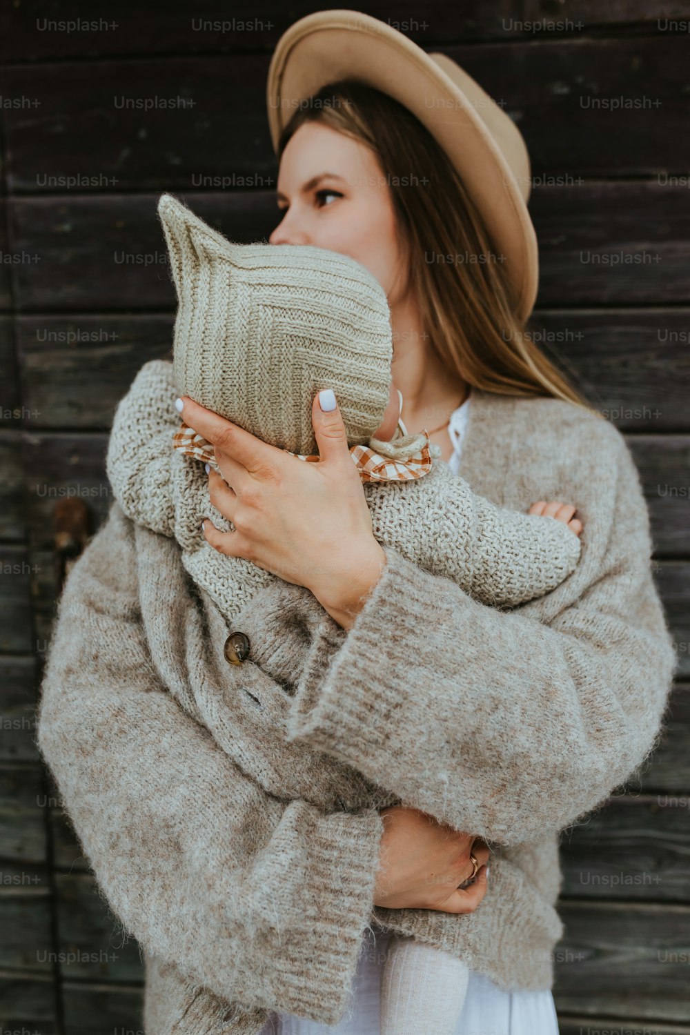 a woman in a hat and sweater holding a cat pillow