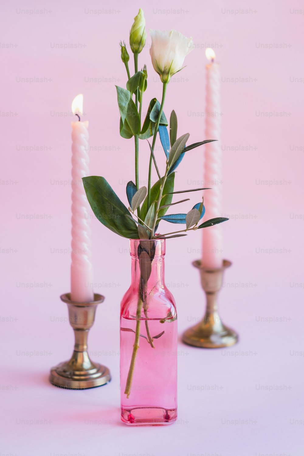 Un jarrón rosa lleno de flores junto a dos velas