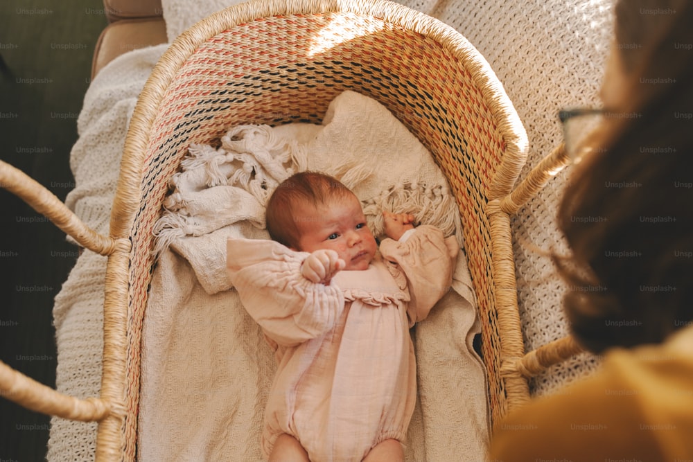 un bébé allongé dans un panier en osier à côté d’une femme