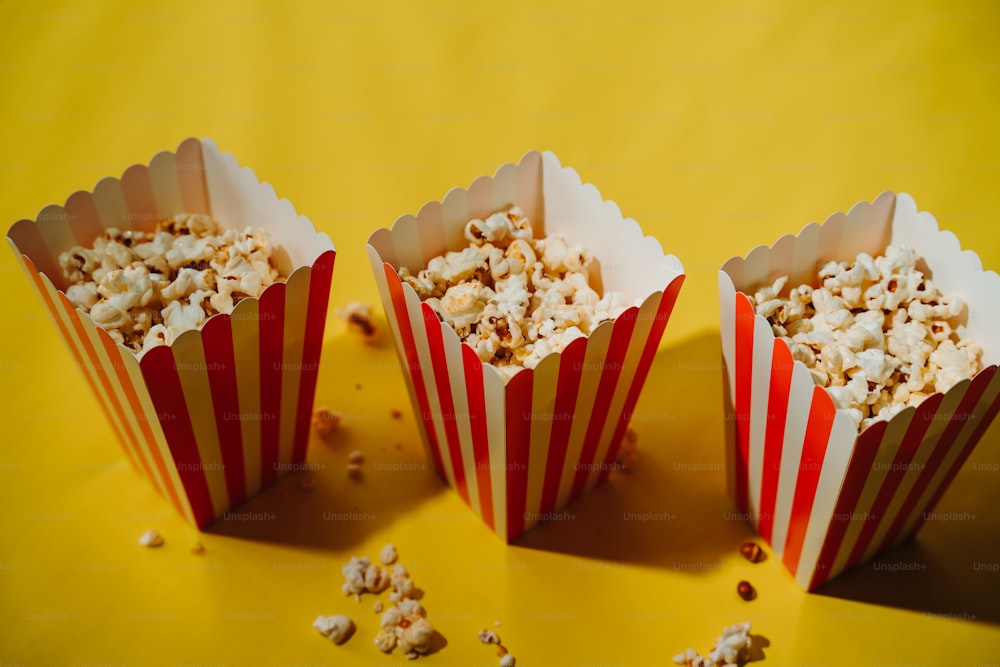 Tre bicchieri di carta a strisce rosse e bianche pieni di popcorn