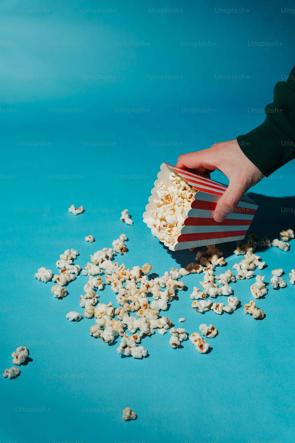 a person holding a popcorn box over a pile of popcorn