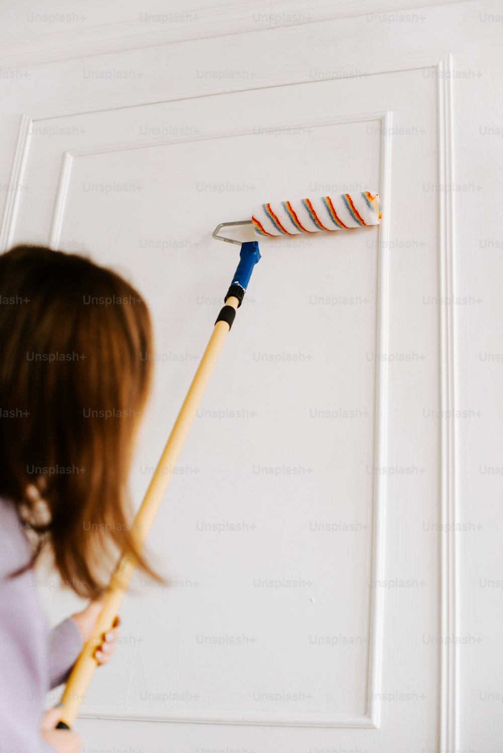 a little girl holding a paintbrush in front of a white door