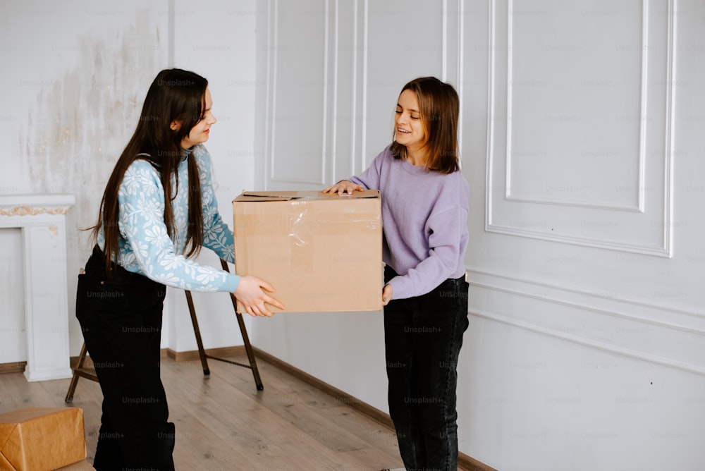 two girls are holding a cardboard box in a room