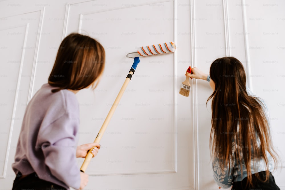 two young girls painting a wall with paint rollers