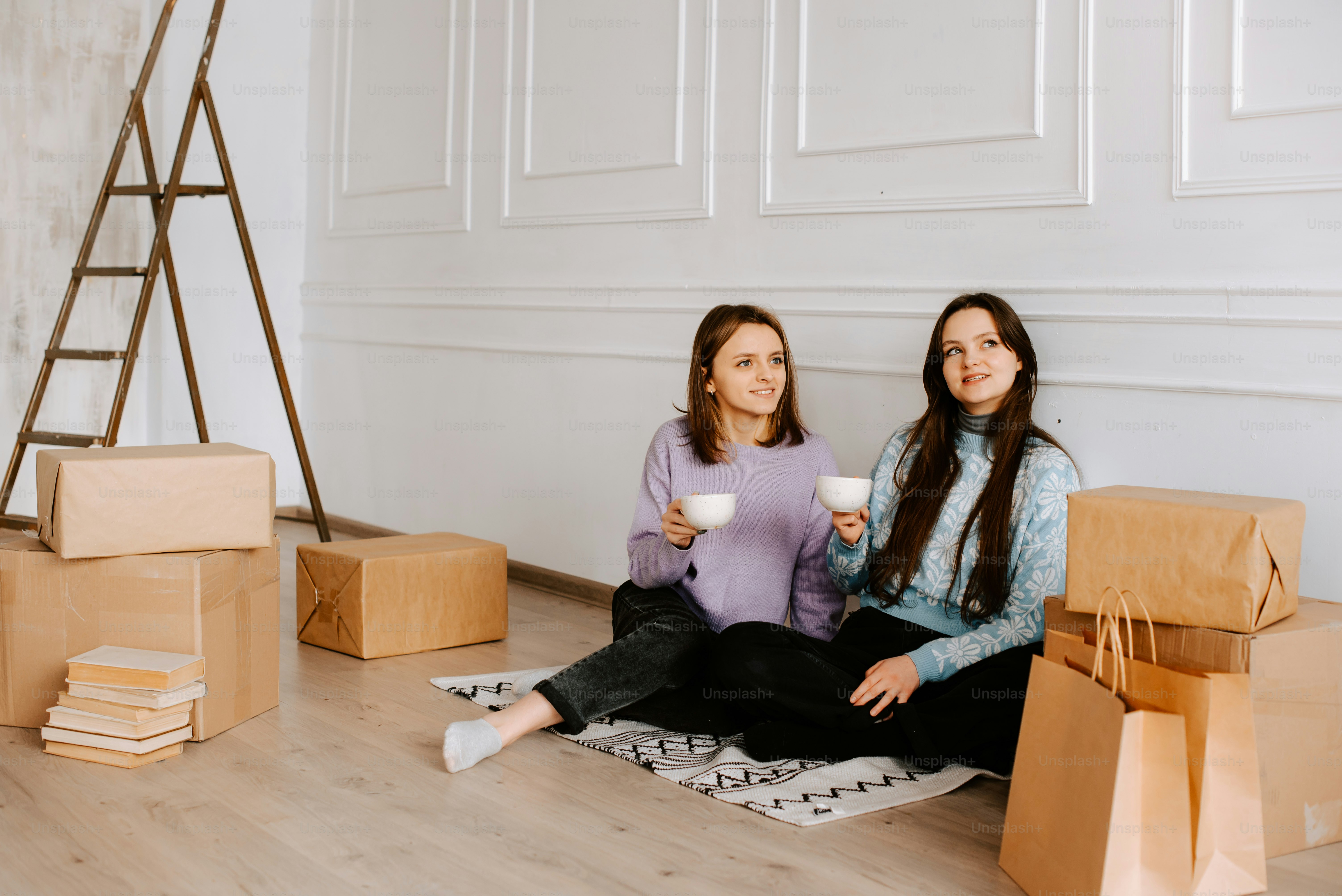 two women sitting on the floor holding cups of coffee