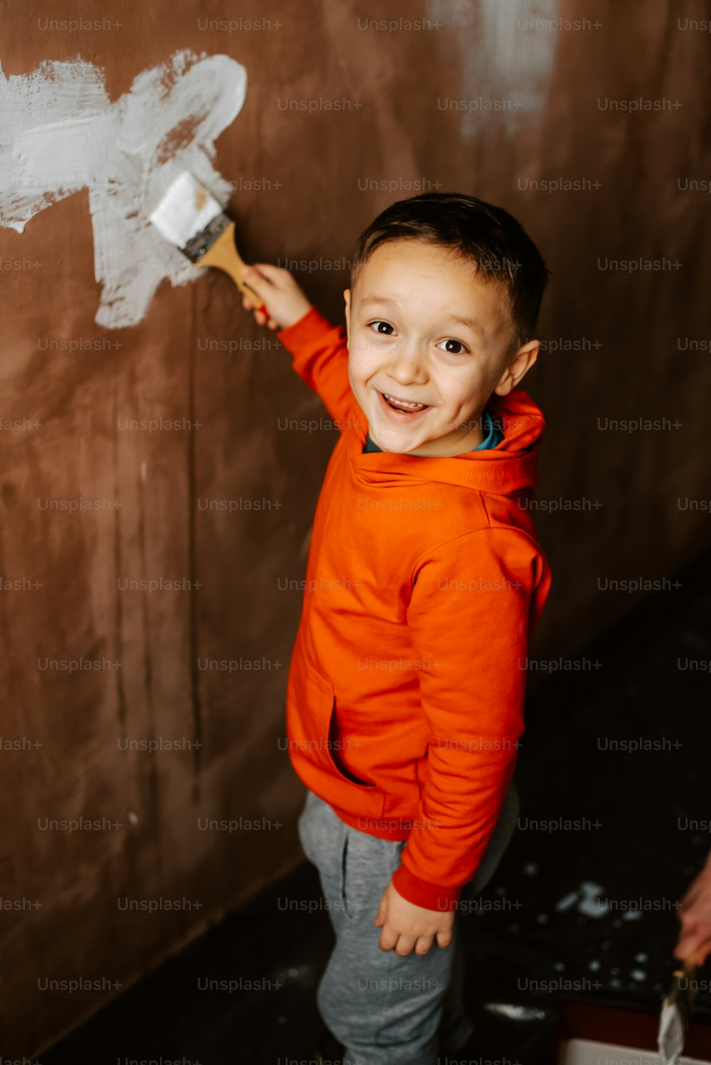 um menino em pé na frente de uma parede com um pincel