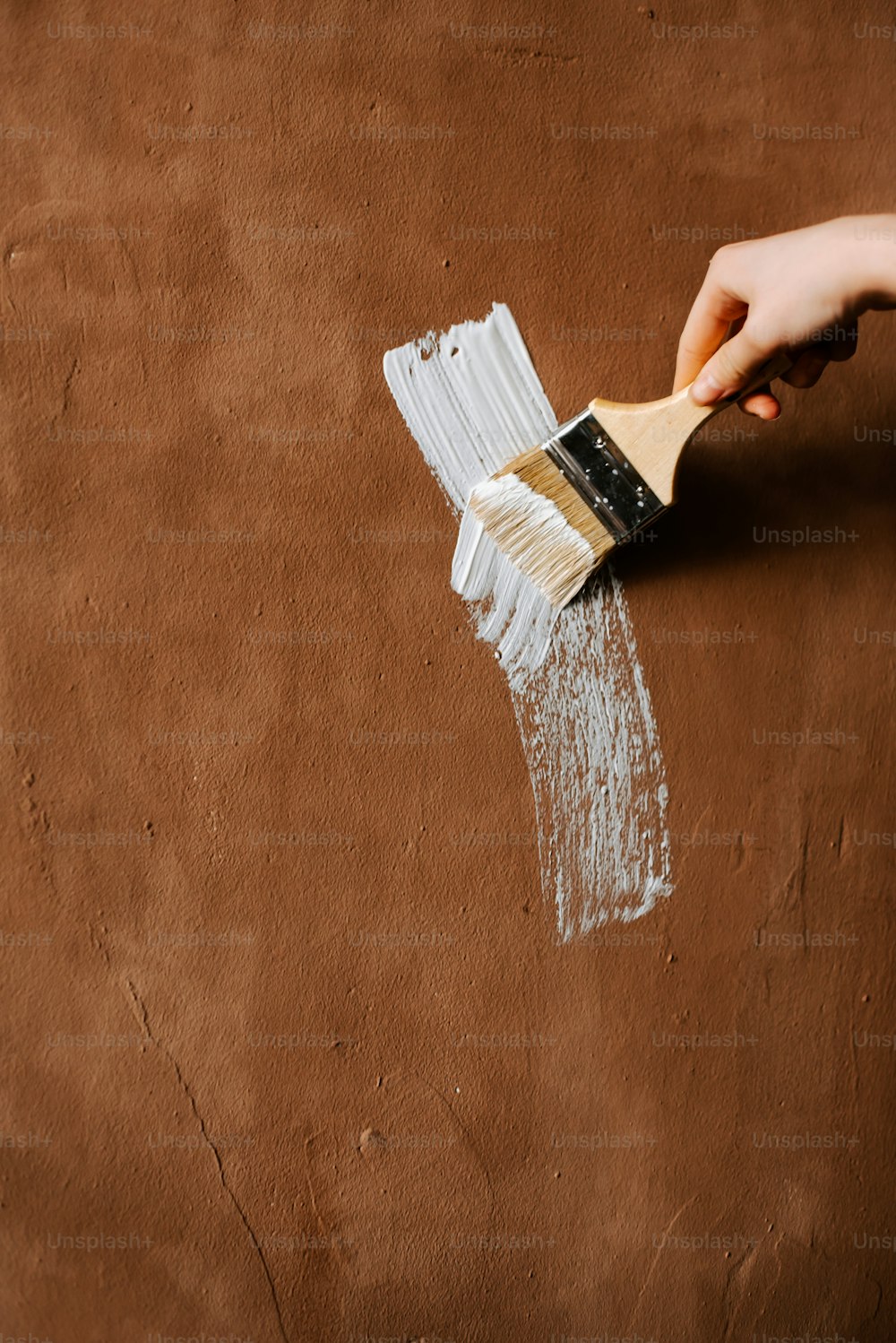 a person holding a paint brush over a brown surface
