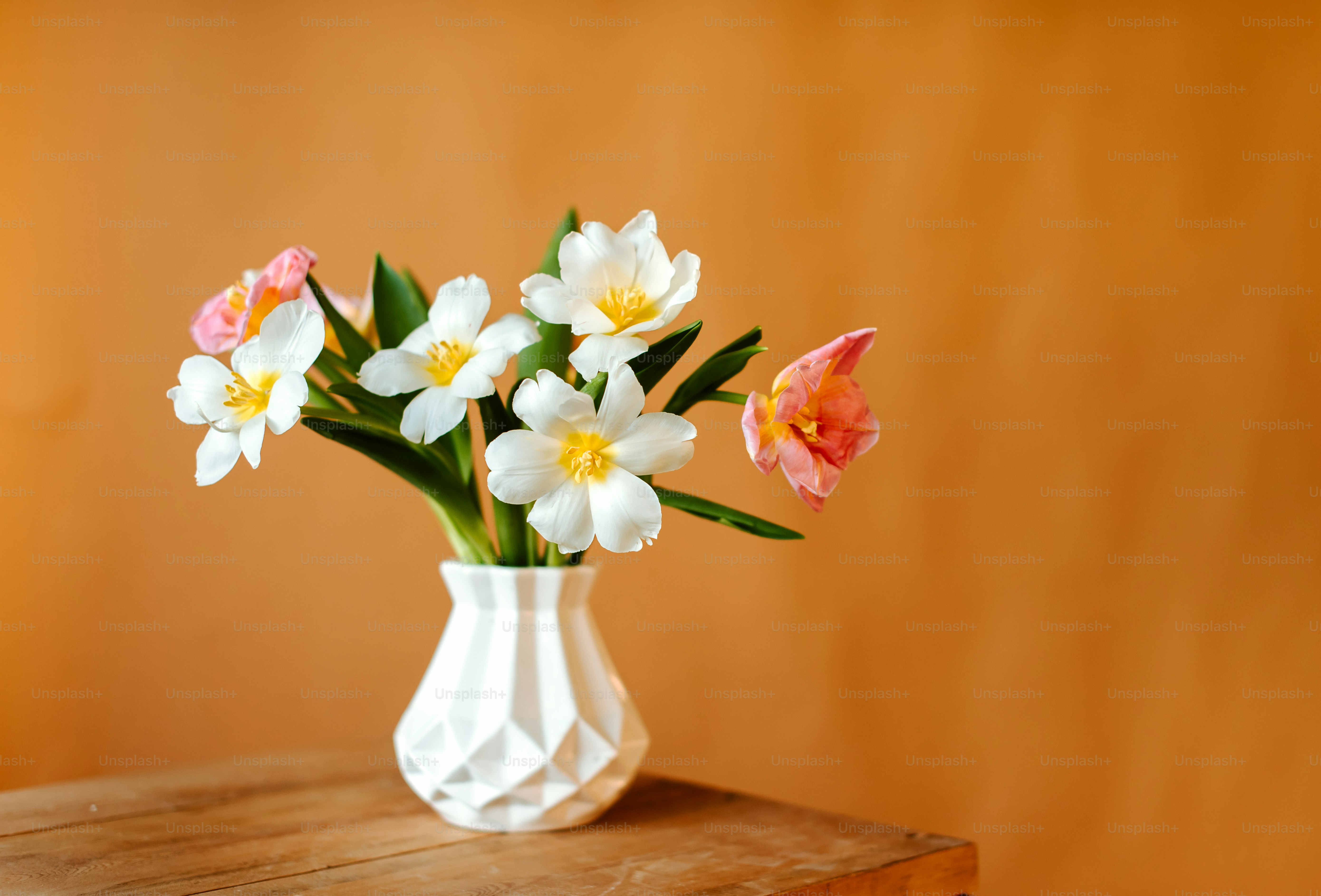 eine weiße Vase gefüllt mit Blumen auf einem Holztisch